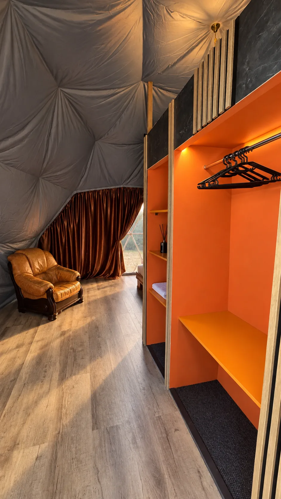 Гардеробная зона с открытым шкафом и креслом внутри геокупола Skala River Retreat